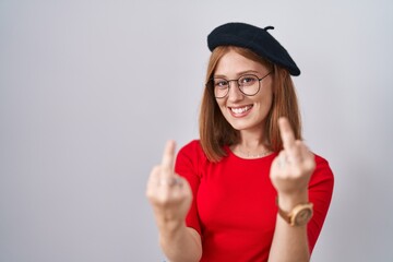 Young redhead woman standing wearing glasses and beret showing middle finger doing fuck you bad...
