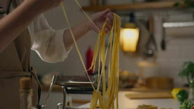 Italian, housewife woman immersed Checks looks at spaghetti from raw dough specialized cooking shop. Camera in motion Skilled worker Rolling out dough mastering healthy eating skills, raw spaghetti
