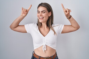 Young beautiful woman wearing casual white t shirt smiling amazed and surprised and pointing up with fingers and raised arms.