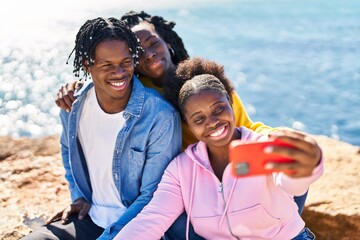 African american friends making selfie by the smartphone sitting on rock at seaside