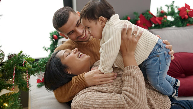 Couple and son hugging each other sitting on sofa by christmas tree at home
