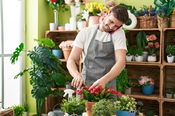 Young caucasian man florist talking on smartphone cutting plant at flower shop