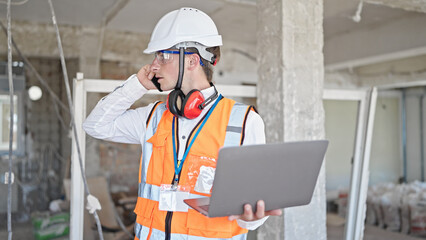 Naklejka na ściany i meble Young caucasian man architect talking on smartphone using laptop at construction site