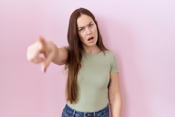 Beautiful brunette woman standing over pink background pointing displeased and frustrated to the camera, angry and furious with you