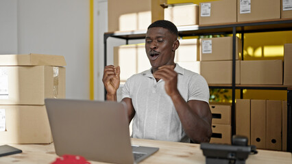 African american man ecommerce business worker typing on laptop with winner gesture at office
