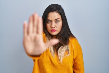 Young hispanic woman standing over isolated background doing stop sing with palm of the hand....