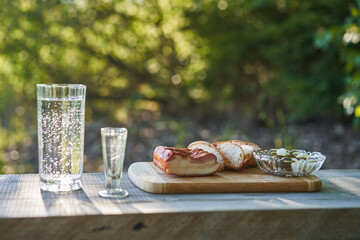 Typical slavic style snack consist from smoked pork bacon, a few slices for rustic bread, pickled sweet and saur cucumbers and shot of vodka and glass of pring water served outside on wooden plate.