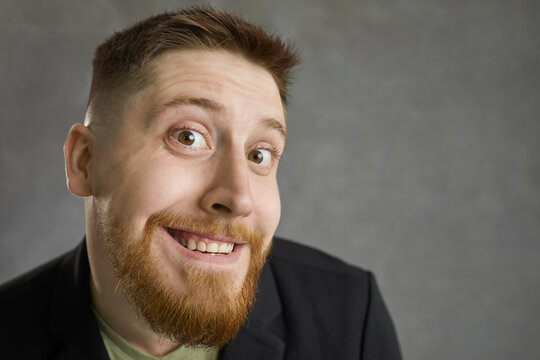 Feeling and emotions. Close up of funny face of happy emotional young caucasian man on gray background. Cheerful man grimaces funny in front of the camera. Facial expressions concept.