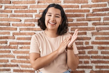 Young hispanic woman standing over bricks wall clapping and applauding happy and joyful, smiling proud hands together
