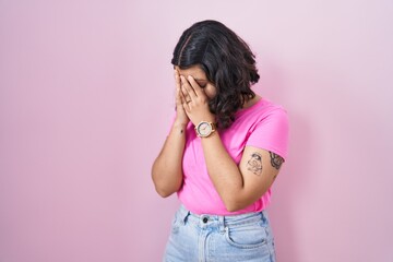 Young hispanic woman standing over pink background with sad expression covering face with hands...