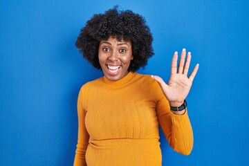 Fototapeta na wymiar Black woman with curly hair standing over blue background showing and pointing up with fingers number five while smiling confident and happy.