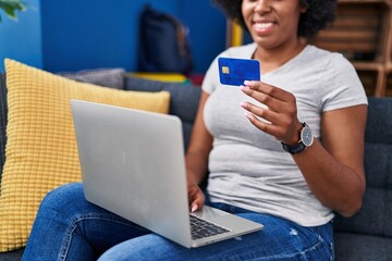 African american woman using laptop and credit card sitting on sofa at home