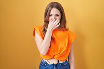Caucasian woman standing over yellow background smelling something stinky and disgusting, intolerable smell, holding breath with fingers on nose. bad smell
