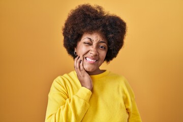 Fototapeta na wymiar Young african american woman standing over yellow background touching mouth with hand with painful expression because of toothache or dental illness on teeth. dentist