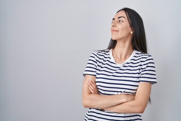 Fototapeta premium Young brunette woman wearing striped t shirt looking to the side with arms crossed convinced and confident