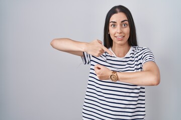 Young brunette woman wearing striped t shirt in hurry pointing to watch time, impatience, upset and...
