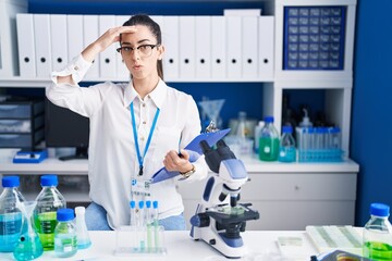 Young brunette woman working at scientist laboratory worried and stressed about a problem with hand...