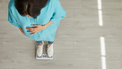 Top view portrait of a young pregnant woman wearing homewear measuring her weight standing on a...