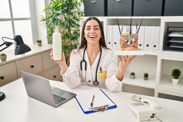 Hispanic doctor woman holding model of human anatomical skin and hair smiling and laughing hard out...