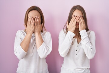 Middle age mother and young daughter standing over pink background rubbing eyes for fatigue and...