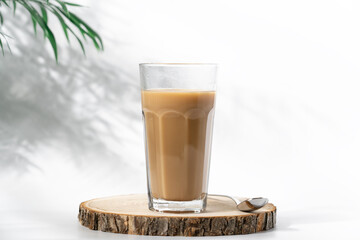 Coffee with milk in tall glass. Coffee on wooden podium close up view on white background with shadow