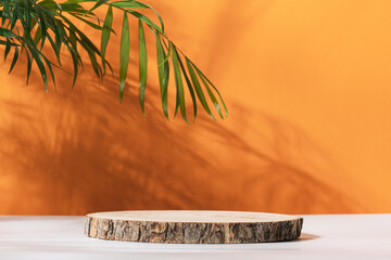 Wooden cut podium on orange background with palm tree shadow. Stand for the presentation of beauty...