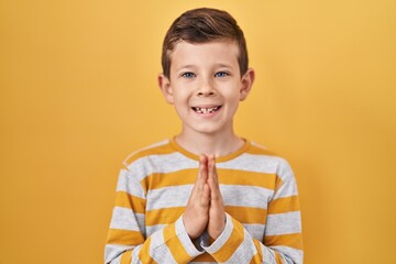 Young caucasian kid standing over yellow background praying with hands together asking for...
