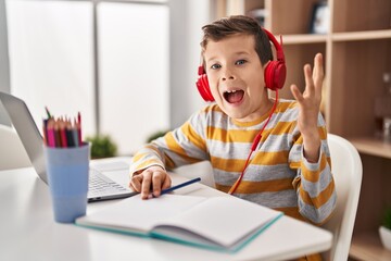 Young caucasian kid doing homework at home celebrating victory with happy smile and winner...