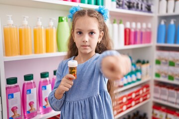 Young little girl holding pills at the pharmacy pointing with finger to the camera and to you, confident gesture looking serious