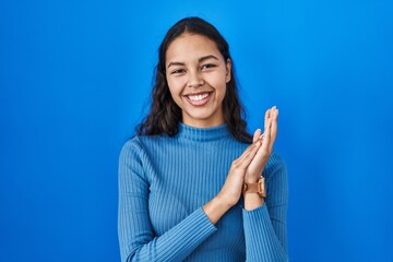 Young brazilian woman standing over blue isolated background clapping and applauding happy and...