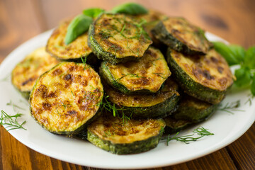zucchini fried in circles with spices and herbs, in a plate .