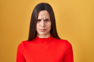 Fototapeta premium Young hispanic woman standing over yellow background skeptic and nervous, frowning upset because of problem. negative person.