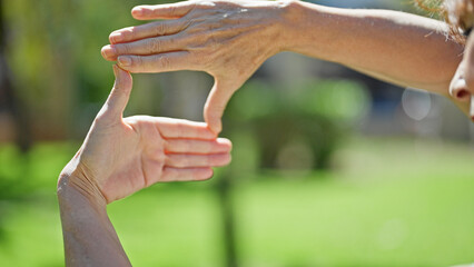 Middle age woman smiling confident doing frame gesture with hands at park