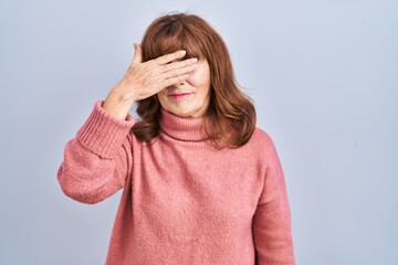 Middle age hispanic woman standing over isolated background covering eyes with hand, looking...