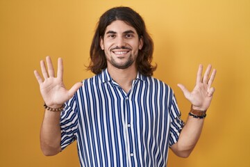 Hispanic man with long hair standing over yellow background showing and pointing up with fingers...