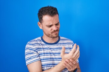 Naklejka premium Young hispanic man standing over blue background suffering pain on hands and fingers, arthritis inflammation