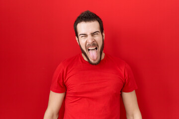 Young hispanic man wearing casual red t shirt sticking tongue out happy with funny expression. emotion concept.