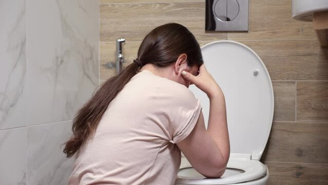 Woman feels nauseous sitting near toilet in bathroom. Feeling unwell after spending time at party. Consequences of drinking alcohol backside view