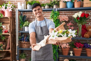 Young hispanic man florist holding bouquet of flowers at flower shop
