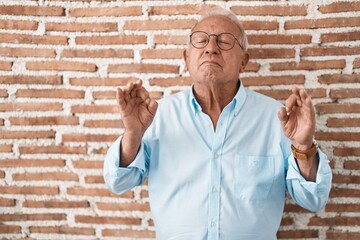 Senior man with grey hair standing over bricks wall relaxed and smiling with eyes closed doing...