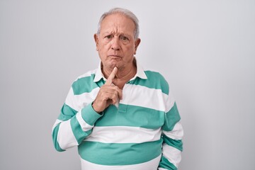 Senior man with grey hair standing over white background thinking concentrated about doubt with finger on chin and looking up wondering