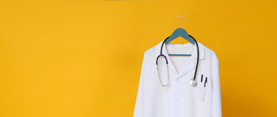 White coat of a doctor with a stethoscope on a yellow background, place for text