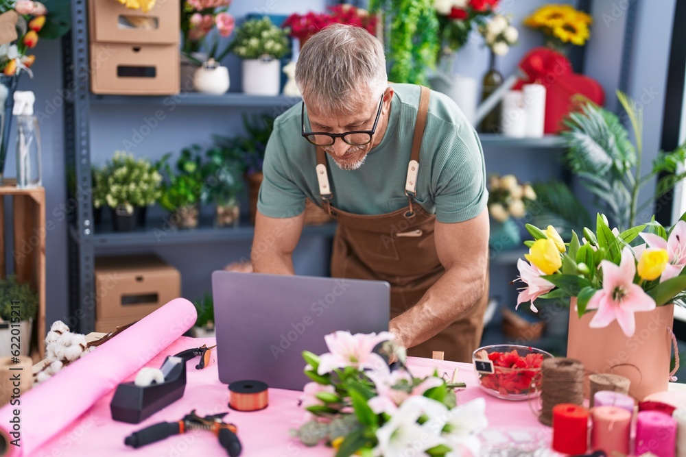 Sticker middle age grey-haired man florist using laptop standing at flower shop