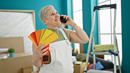 Middle age grey-haired woman talking on smartphone choosing color at new home