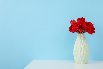 A vase with tulips on the table, on a blue background