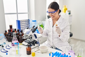 Young beautiful hispanic woman scientist holding liquid and tweezers at laboratory