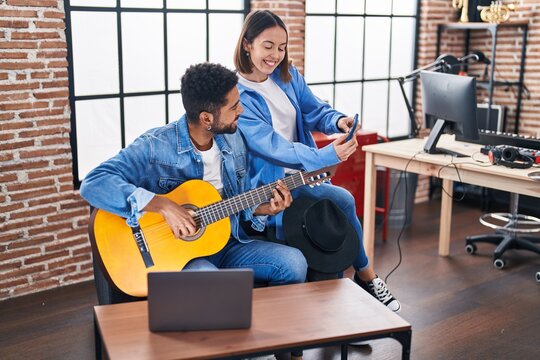 Man and woman musicians playing classical guitar using smartphone at music studio