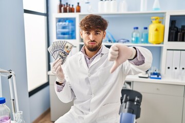 Arab man with beard working at scientist laboratory holding money with angry face, negative sign...