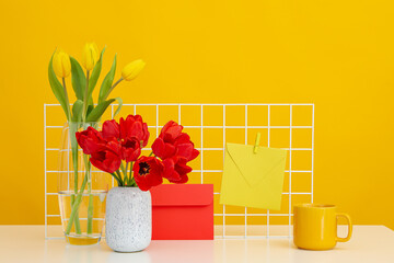 A desk with flowers, letters and a cup on a yellow background