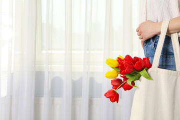 Tulips in a shopper on a girl's hand near the window